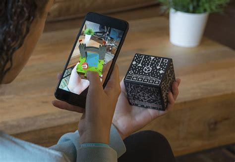 enfant tenant pointant un merge cube avec son smartphone. Image en réalité augmentée sur l"écran de son téléphone.