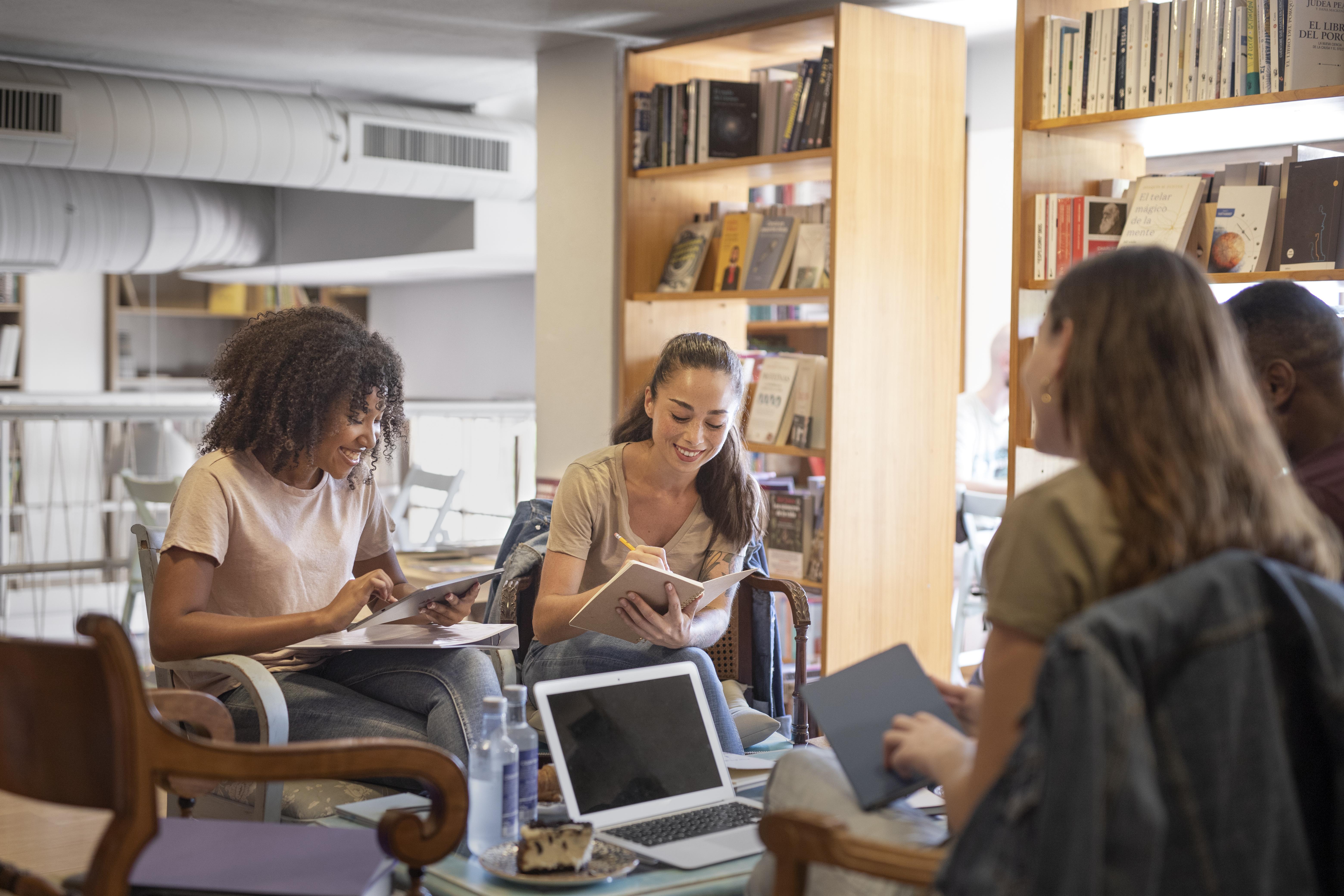 uatre personnes assises autour d’une table dans un espace de bibliothèque. Elles échangent et travaillent ensemble dans une ambiance détendue.
