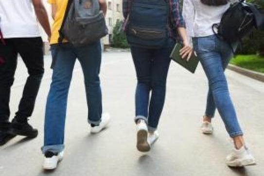Des jeunes, vus de dos, marchent dans une même direction sur une route